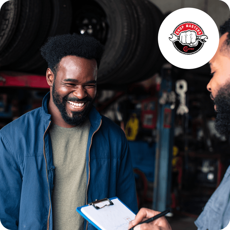 Two men in a garage smiling; one holds a clipboard. Shelves with tires are visible in the background. A "Shop Masters" logo is on the top right.
