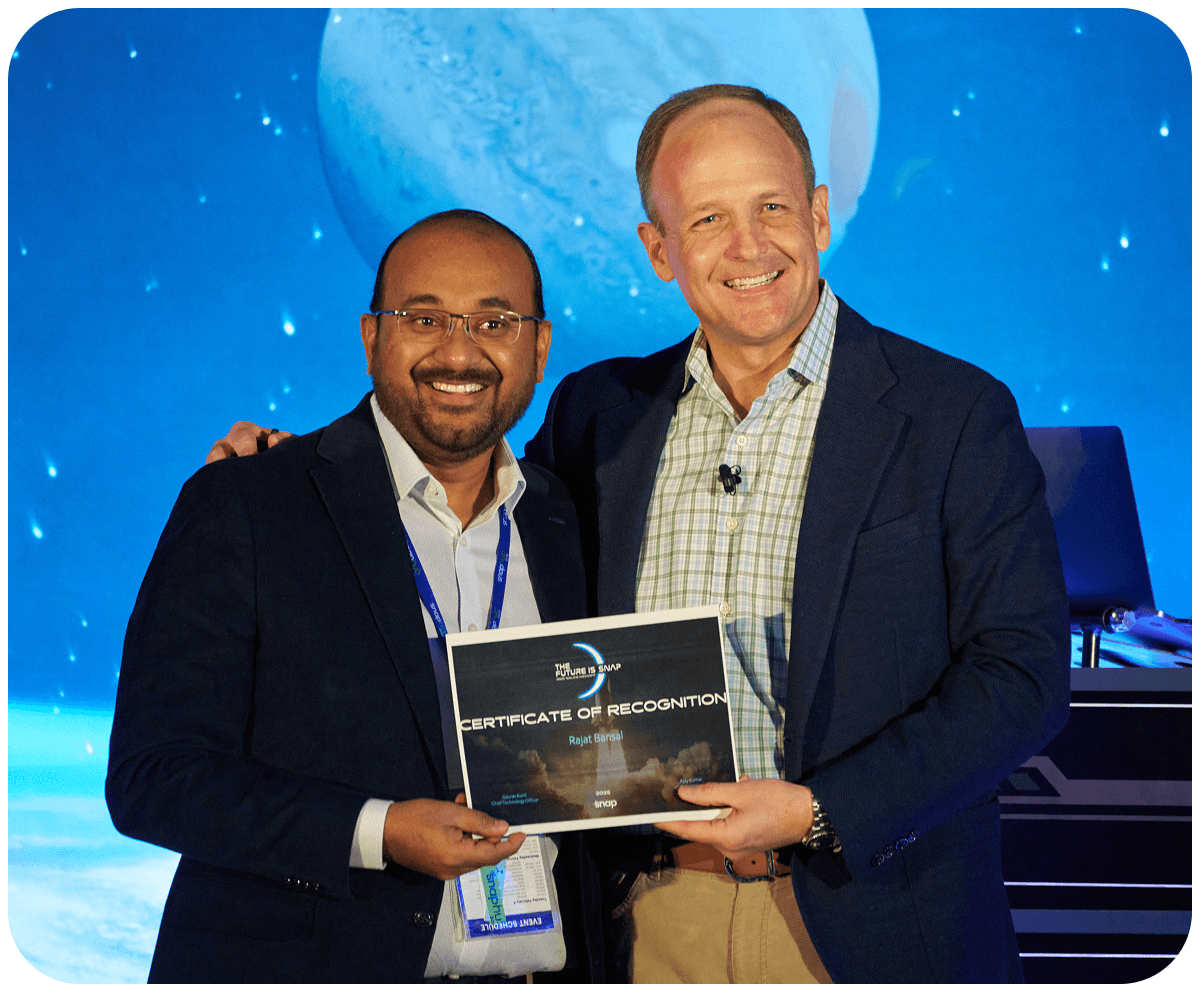 Two men smiling, holding a certificate of recognition on stage with a blue, planetary backdrop.