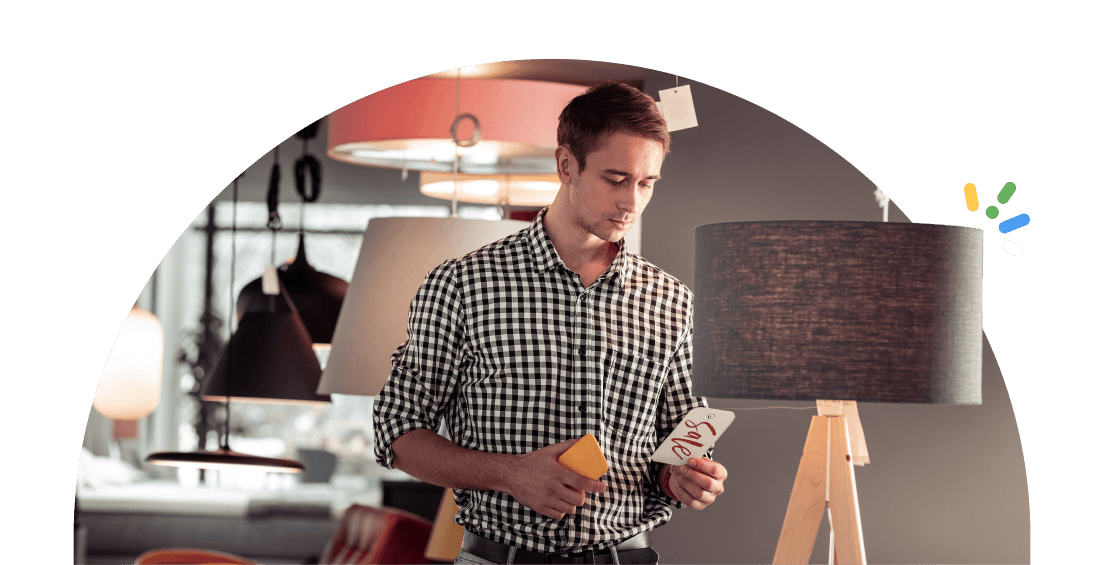 A man in a furniture store room looking at a price tag attached to a grey lamp
