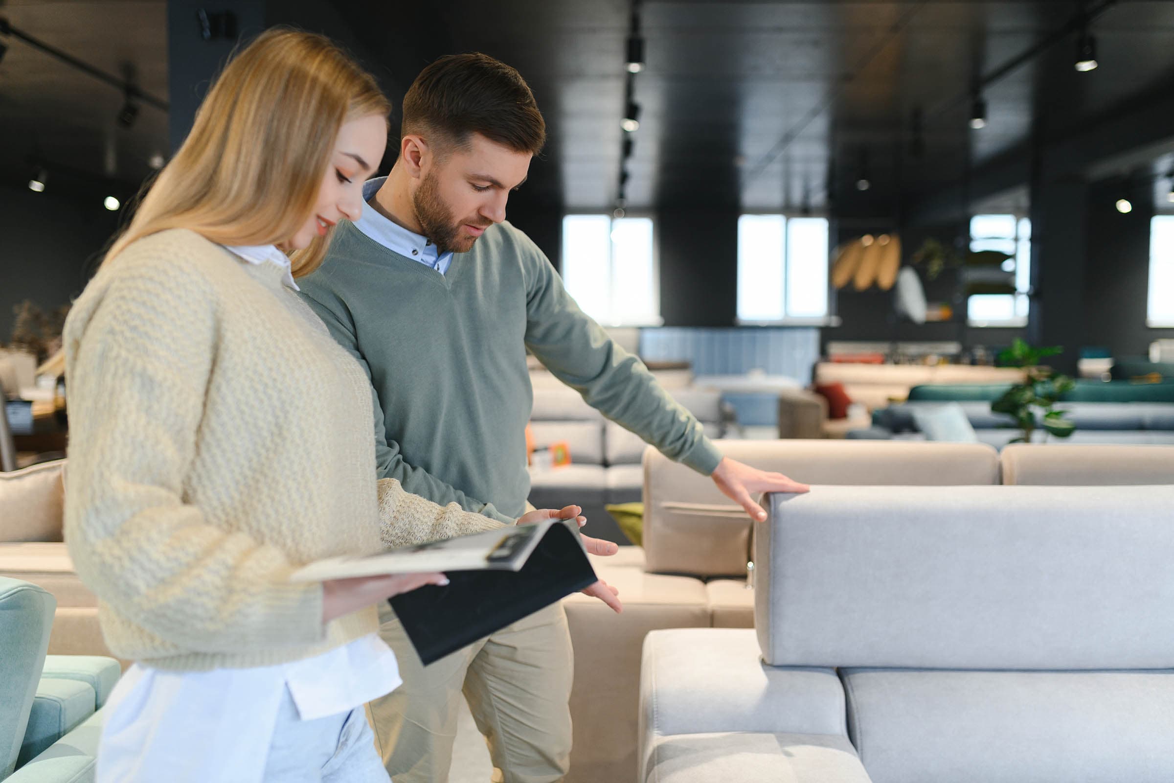 A man and a woman in a furniture store discuss a gray sofa, with various other couches in the background.