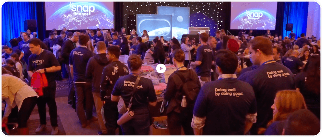A crowded event with people wearing "Doing well by doing good" shirts, gathering under a starry backdrop with "Snap Finance" displays.