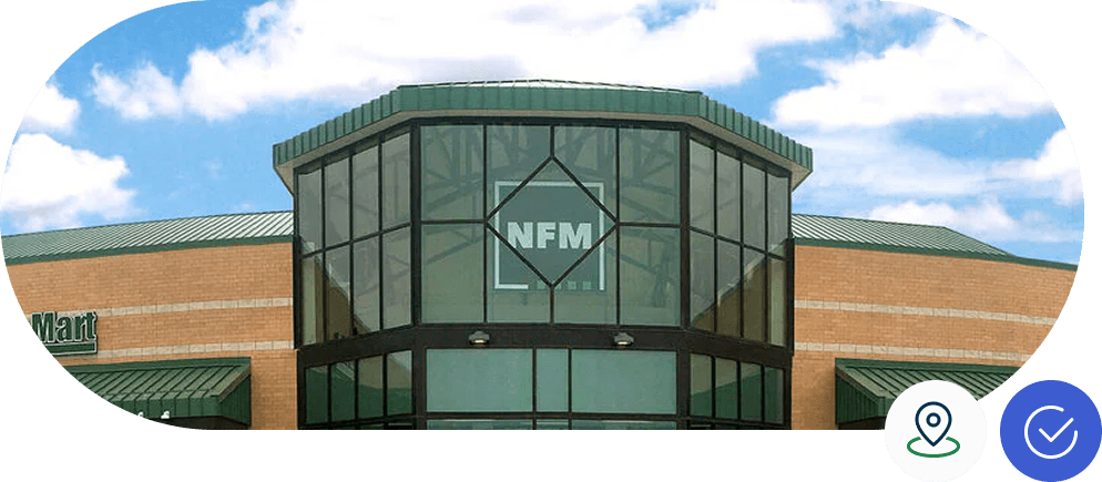 Building with a glass entrance displaying "NFM" against a clear blue sky. A brick structure with green roofing surrounds the entrance.