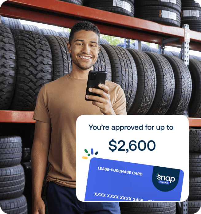 A man looking at his phone in a tire shop. Overlaid is a card that says "You're approved for up to $2,600."