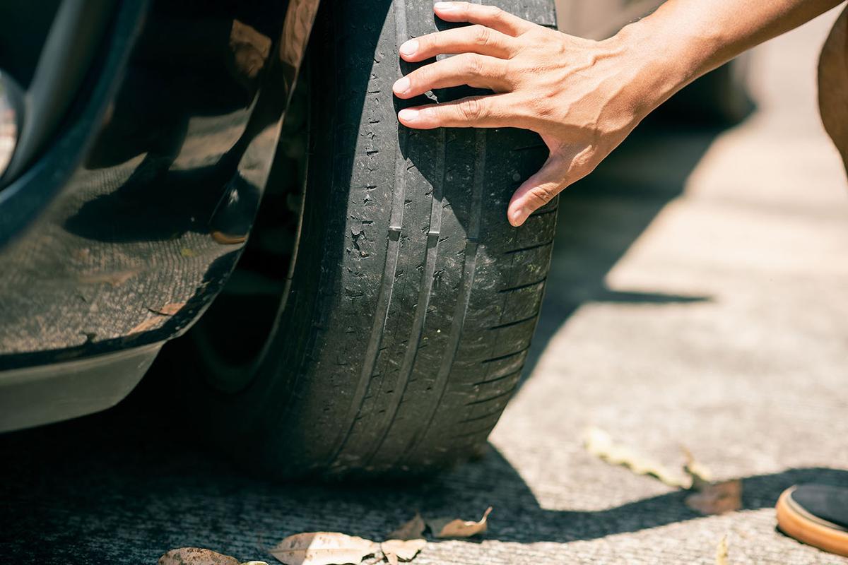 Close-up of a hand feeling a bald, cracked car tire, highlighting severely worn tread on a parked vehicle.