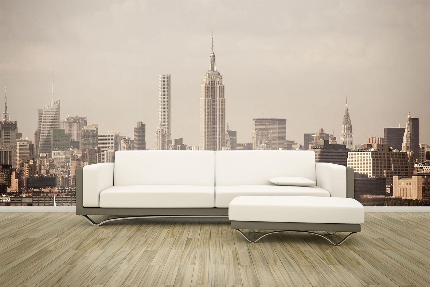 Modern white sectional sofa on light wood floor, set against a wall mural of New York City skyline with the Empire State Building centered.