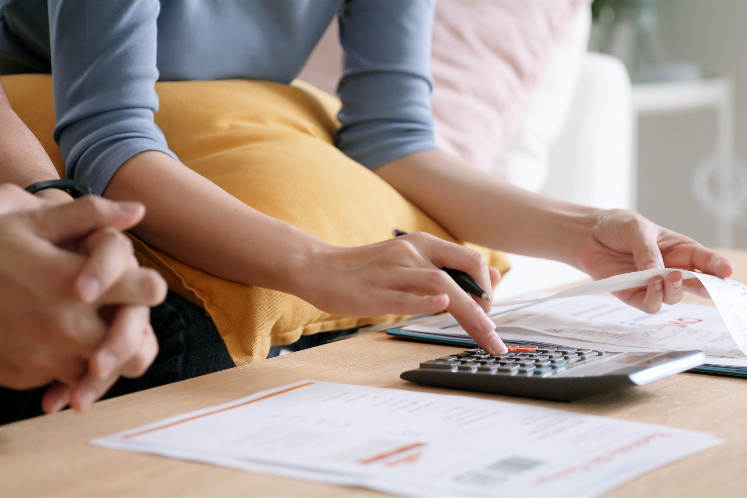 Close-up of two people reviewing finances at a table, with one person using a calculator and holding a receipt.