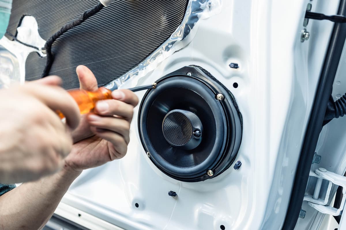 Hands using a screwdriver to install a round speaker in a car door panel.
