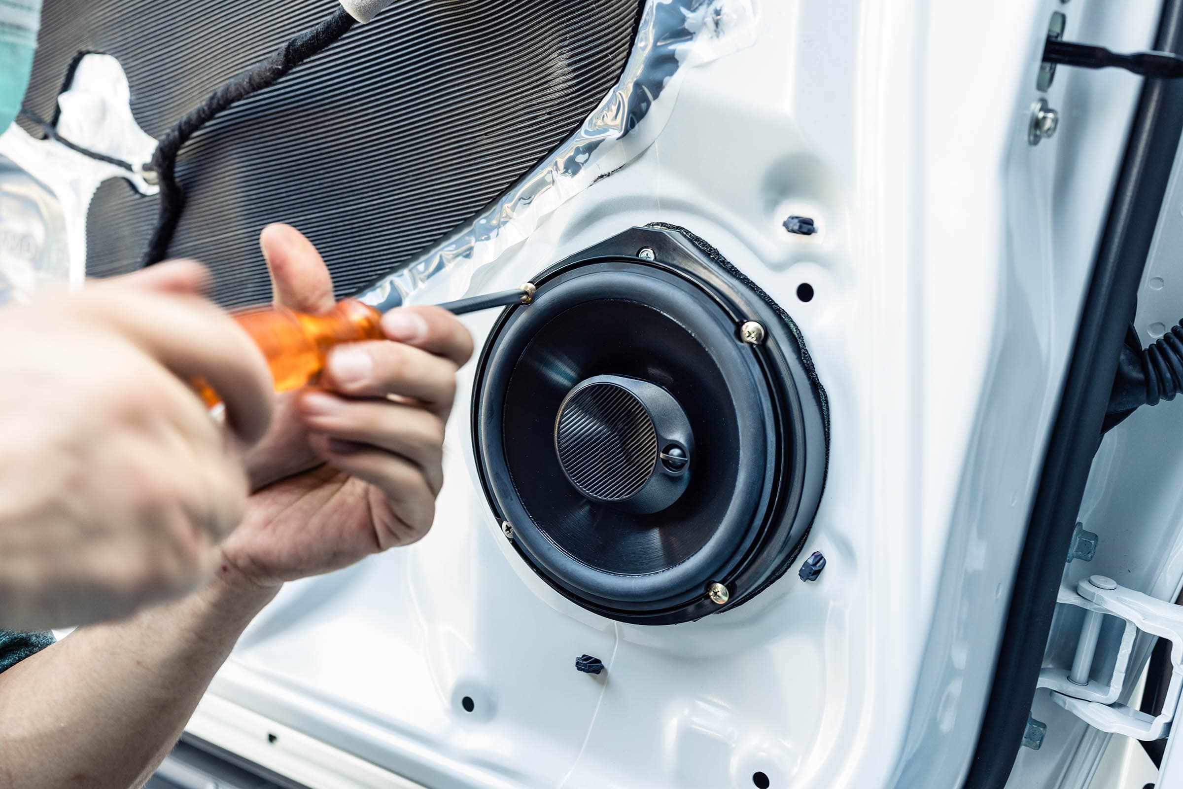 Hands using a screwdriver to install a round speaker in a car door panel.