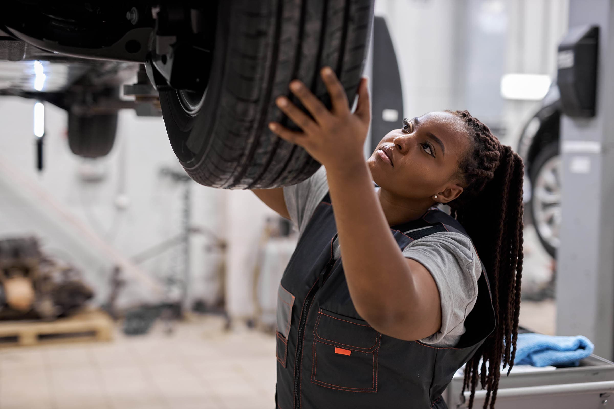 Mechanic inspecting a car tire in a workshop, focused and checking for details with tools and equipment in the background.