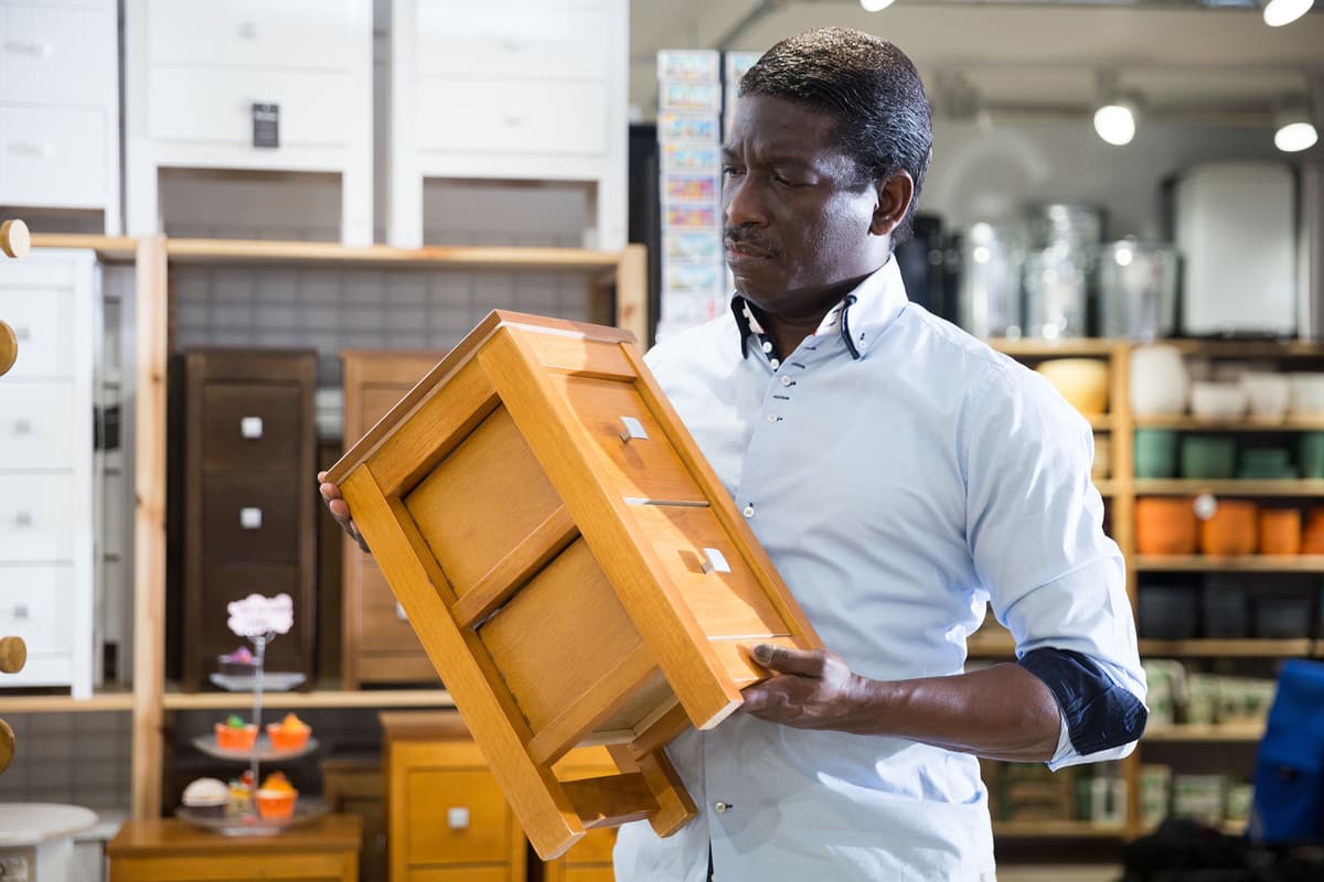 A person examines a small wooden cabinet in a home goods store, with various shelves and containers in the background.