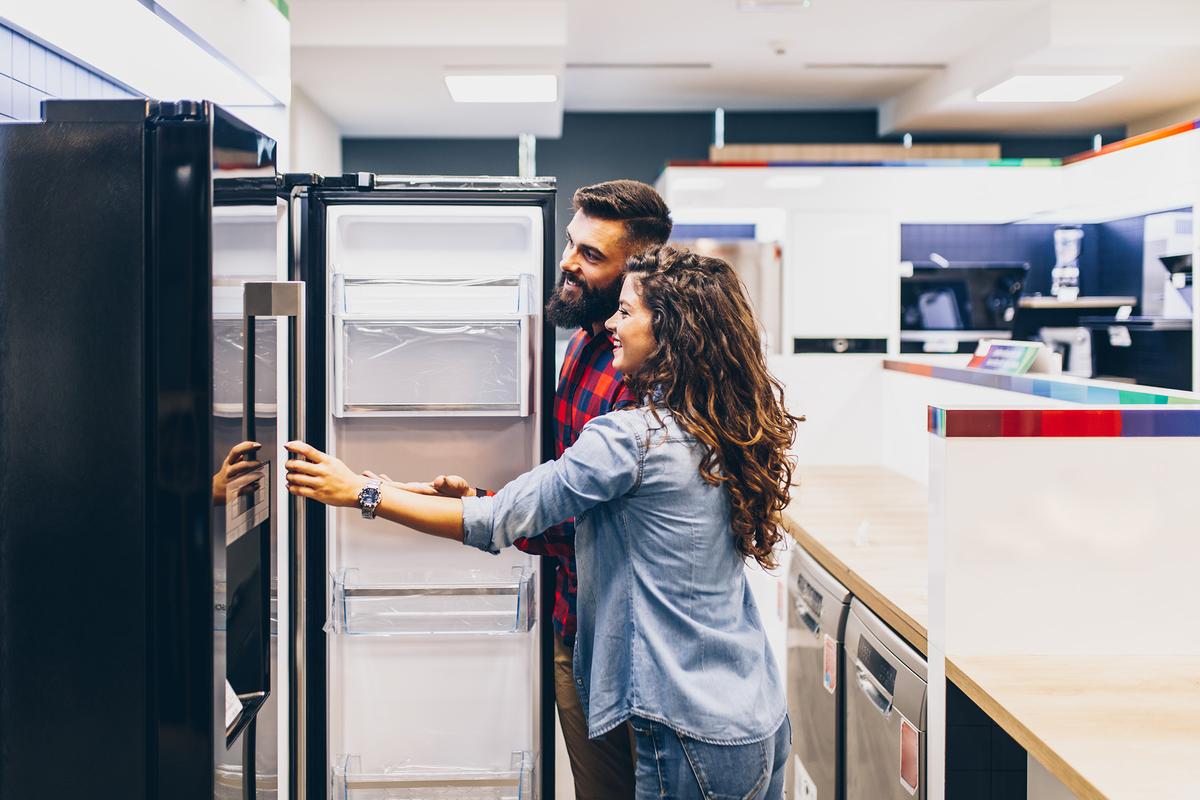 Smiling couple inspecting the inside of an open refrigerator in an appliance store showroom.