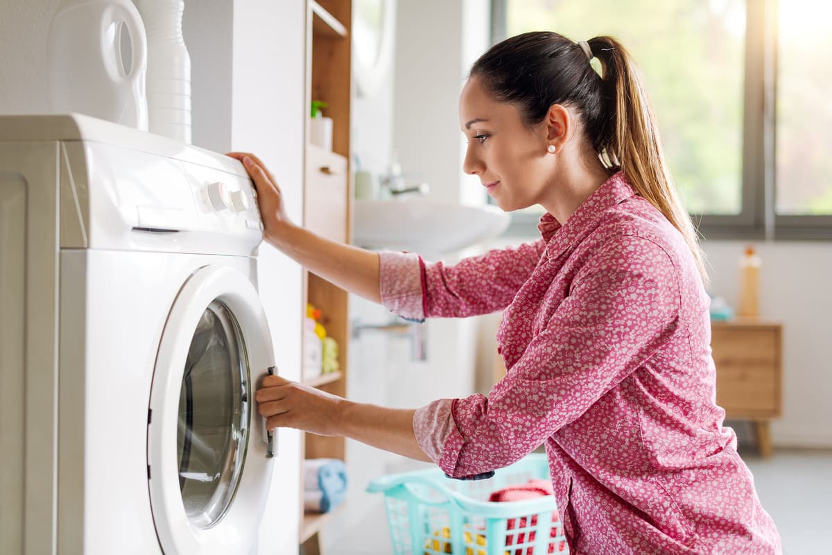 Woman in a pink shirt using a front-loading washing machine in a bright laundry room.
